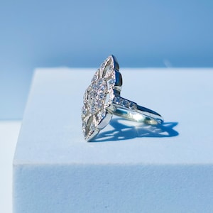 Puede incluir: Un anillo de plata con una piedra grande, clara y facetada rodeada de piedras más pequeñas en un diseño floral.