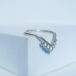 May include: A silver ring with a V-shaped design and a row of small, round beads at the bottom.