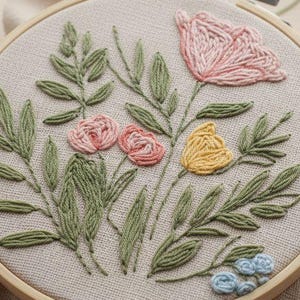 May include: An embroidery hoop with a floral design in pink, yellow, and blue, with green leaves. The embroidery is set in a wooden hoop and rests on a beige fabric. Several embroidery tools are scattered around the hoop.