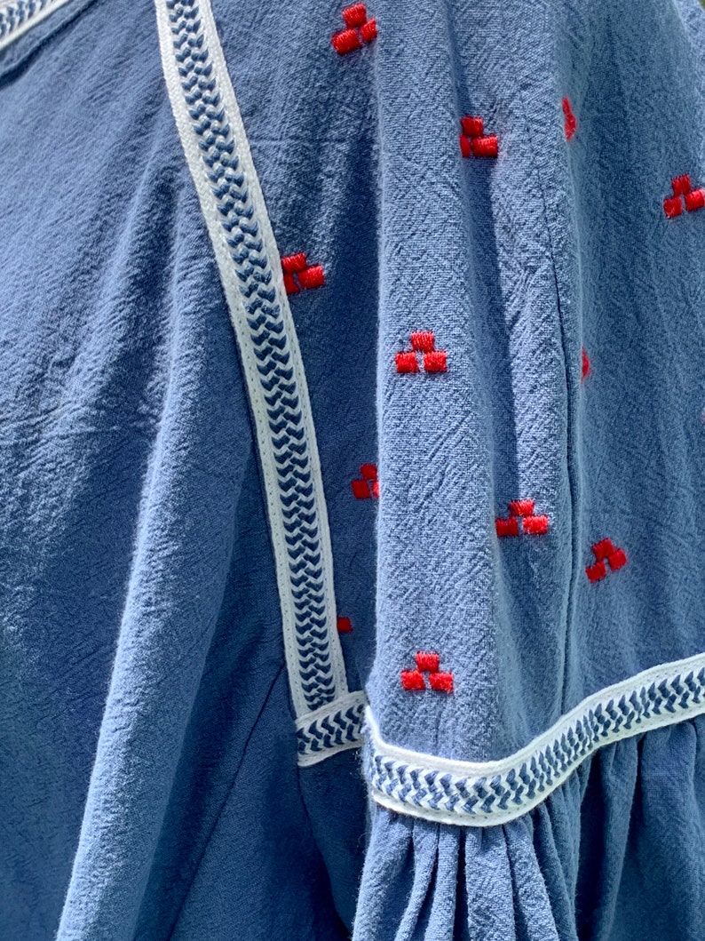 May include: A blue cotton shirt with white and blue trim and red embroidered details.