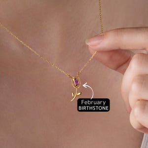 May include: A gold chain necklace with a rose pendant featuring a purple birthstone. The pendant is labeled "February Birthstone".