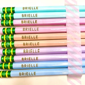 May include: A set of ten pencils with a green and yellow striped band and the name "Brielle" printed in gold on each pencil. The pencils are in a variety of pastel colors, including light blue, pink, and lavender.