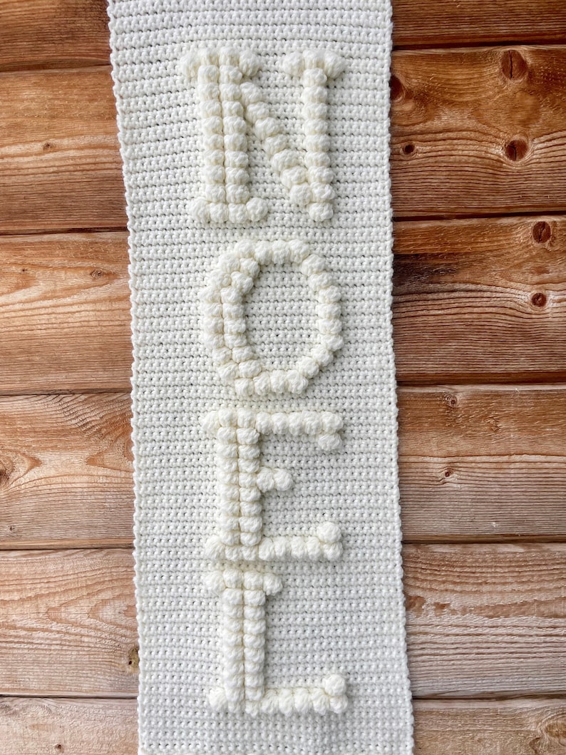 May include: White crocheted wall hanging with the word "NOEL" spelled out in raised letters.
