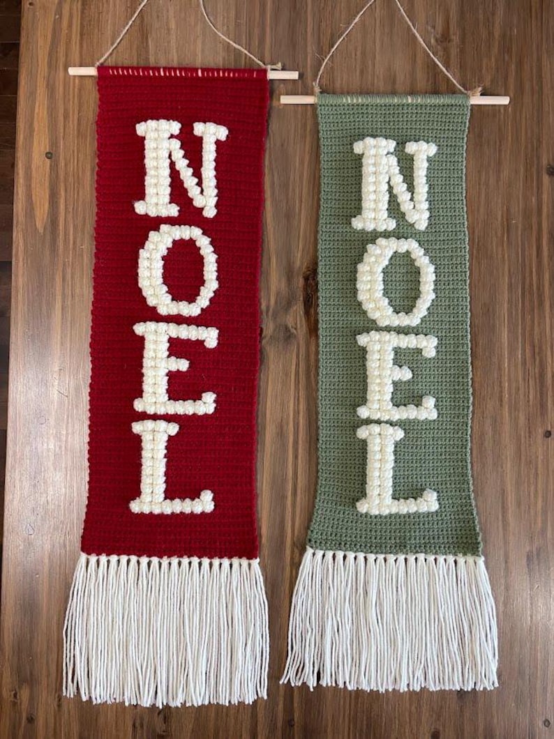 May include: Two crocheted wall hangings with the word "NOEL" spelled out in white yarn on a red and green background. Each hanging has a white fringe at the bottom.