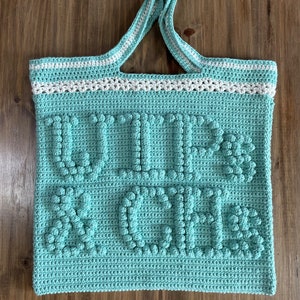 May include: A teal crocheted tote bag with white trim and the words "Wild & Free" in raised lettering.