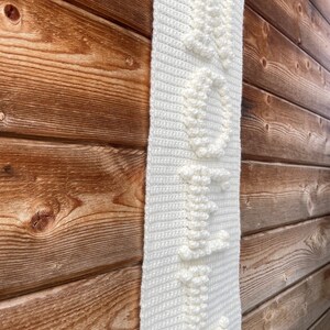 May include: White crocheted wall hanging with a textured design. The hanging features a fringe at the bottom.