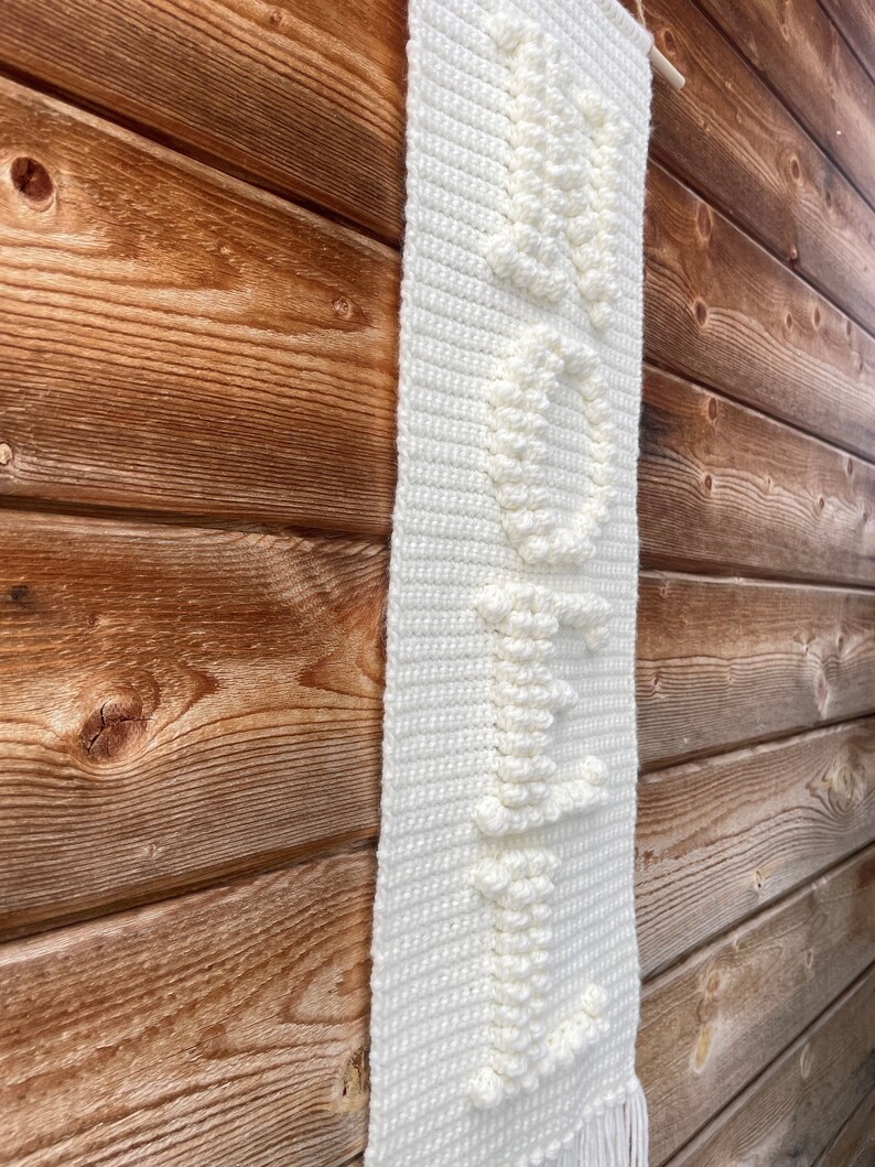 May include: White crocheted wall hanging with a textured design. The hanging features a fringe at the bottom.