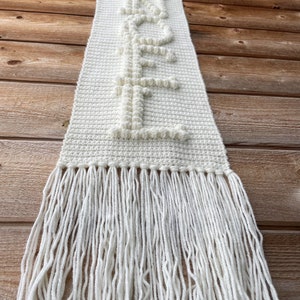 May include: White crocheted wall hanging with the word "HOPE" spelled out in raised letters. The hanging has a fringe border.