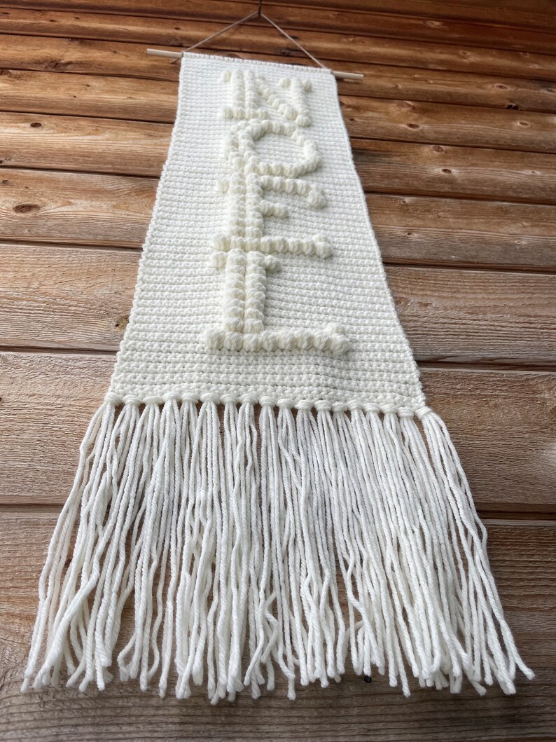 May include: White crocheted wall hanging with the word "HOPE" spelled out in raised letters. The hanging has a fringe border.