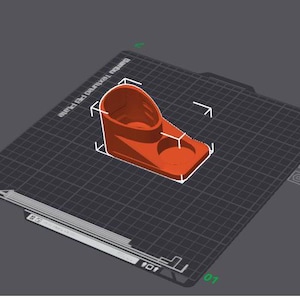 May include: A 3D printed orange plastic object with two circular openings. The object is on a black and white grid surface.