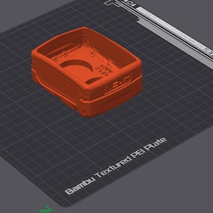 Pode incluir: Um objeto de plástico laranja impresso em 3D com o texto "BAMBU LABS" impresso no lado. O objeto está sobre uma superfície preta texturizada etiquetada como "Bambu Textured PEI Plate".