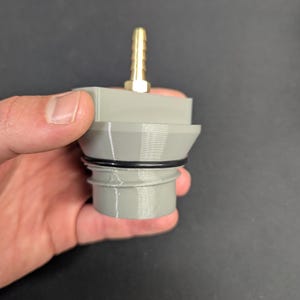 May include: A gray plastic fitting with a brass nozzle. The fitting has a cylindrical base, a black O-ring, and a stepped design leading to the nozzle. The nozzle is gold-colored and has a ribbed surface.