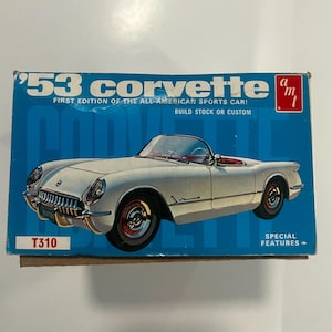 May include: A model kit box for a '53 Corvette, a white sports car with red interior and black tires. The box is blue with white text that reads "'53 Corvette" and "First Edition of the All-American Sports Car!"