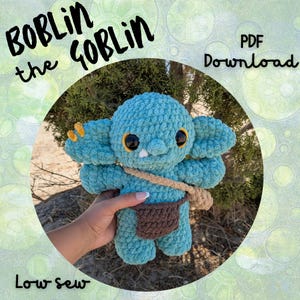 May include: A crocheted teal goblin doll with large ears, big eyes, and a small brown satchel. The doll has a small white tooth and yellow accents. Text on the image reads "Boblin the Goblin", "PDF Download", and "Low sew".