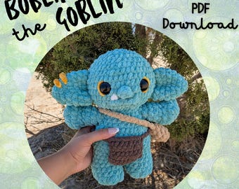 May include: A crocheted teal goblin doll with large ears, big eyes, and a small brown satchel. The doll has a small white tooth and yellow accents. Text on the image reads "Boblin the Goblin", "PDF Download", and "Low sew".