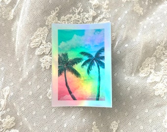 Puede incluir: Una pegatina holográfica con una pintura de acuarela de dos palmeras sobre un cielo de puesta de sol colorido.