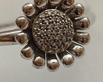 May include: A silver charm bracelet with a flower charm featuring a center of small, clear stones.