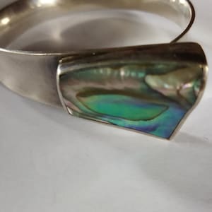 May include: A silver bangle bracelet with a large abalone shell inlay. The shell has iridescent green, blue, and purple colors.