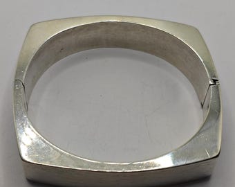 May include: A silver square-shaped bangle bracelet with a hinged closure.