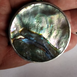 May include: A silver pendant with a round abalone shell inlay. The shell has a swirling pattern of green, blue, and purple.