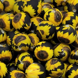 May include: A collection of black and yellow silicone beads with a sunflower pattern. The beads are round and have a hole in the center for stringing.