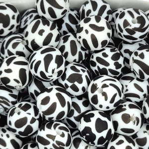 May include: A close-up of a collection of black and white patterned silicone beads. The beads are round and have a smooth, glossy finish.