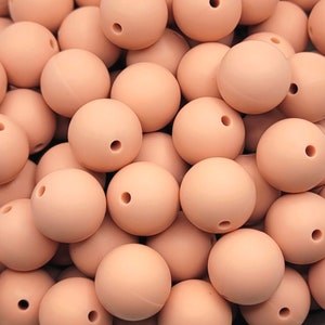 May include: A large pile of blush pink silicone beads. The beads are smooth and round, with a small hole in the center of each bead.