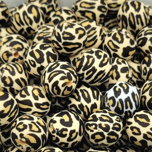 May include: A close-up of a group of round, beige and black beads with a leopard print pattern. The beads are made of wood or plastic and are perfect for crafting jewelry or other projects.