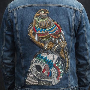 May include: Blue denim jacket with an embroidered design on the back. The design features a colorful eagle perched on a skull, with intricate beadwork in various colors.