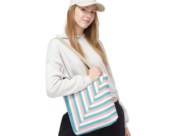 May include: A tote bag with a geometric pattern of alternating stripes in light blue, pink, and white. The bag has a beige shoulder strap and is carried by a person wearing a cream-colored hoodie and a baseball cap.
