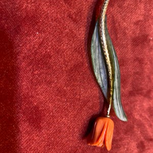 Puede incluir: Broche de tulipán vintage con tallo dorado, flor naranja y hojas verdes. Este broche floral detallado es perfecto para añadir un toque de elegancia inspirada en la naturaleza a cualquier atuendo.