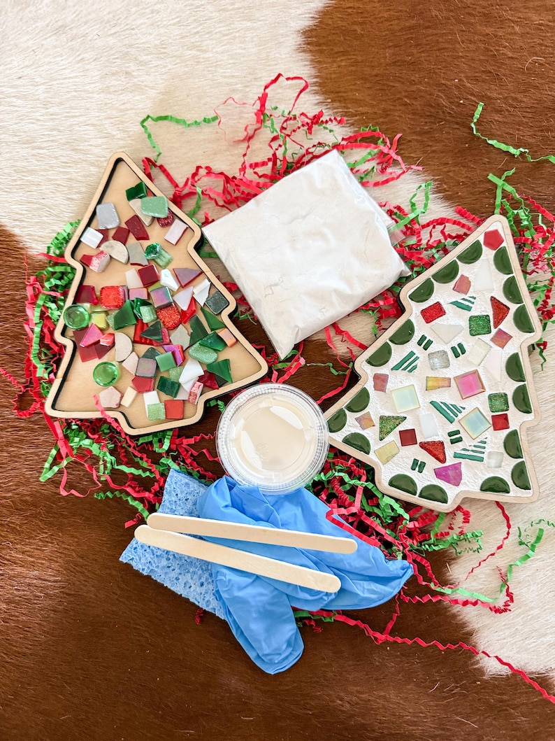May include: A Christmas tree mosaic kit with two wooden tree-shaped bases, colorful mosaic tiles, grout, a sponge, wooden sticks, and blue gloves. The kit includes red and green paper shreds.