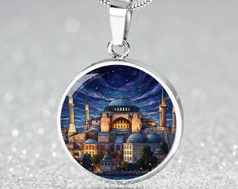 Puede incluir: Collar con colgante plateado con un dije redondo. El dije muestra una colorida ilustración de una ciudad de noche, con cúpulas y minaretes bajo un cielo estrellado. La cadena es plateada.