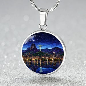 Pode incluir: Colar com pingente prateado com um berloque redondo com um design de paisagem urbana noturna. O berloque mostra um horizonte urbano, montanhas e uma estátua sob um céu estrelado e uma lua crescente. O colar tem uma corrente de cobra.