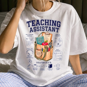 May include: A white t-shirt featuring a graphic print titled Teaching Assistant. The design includes a tote bag filled with school supplies, a multitasking formula, energy level gauge, problem categories chart, and an evolution of a TA timeline.