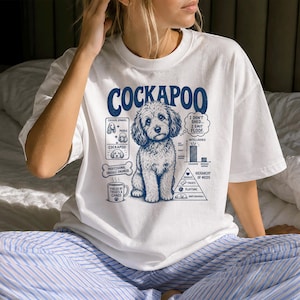 Könnte beinhalten: Ein weißes T-Shirt mit einer blauen Grafik eines Cockapoo-Hundes. Das Design enthält den Text COCKAPOO, I DON'T SHED... I EMIT FLOOF, PROFESSIONAL SNUGGLE ENGINEER, FUELED BY TREATS & CHAOS sowie Diagramme zur Abstammung und den Bedürfnissen.