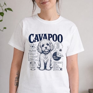 Könnte beinhalten: Ein weißes T-Shirt mit einer dunkelblauen Grafik eines Cavapoo-Hundes, umgeben von wissenschaftlichen und humorvollen Texten, darunter 'Love Particle', ein Tortendiagramm '80% Snuggle', eine Kaffeetasse und eine tägliche Agenda-Liste.