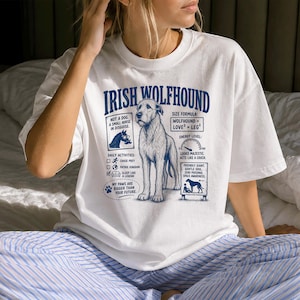 May include: A white short-sleeve t-shirt featuring a blue graphic of an Irish Wolfhound. The design includes text such as IRISH WOLFHOUND, NOT A DOG. A SMALL HORSE IN DISGUISE, SIZE FORMULA: WOLFHOUND = LOVE² + LEG², and MY PAWS ARE BIGGER THAN YOUR FUTURE.