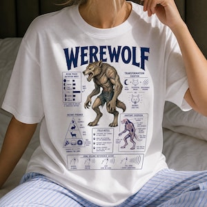 May include: A white t-shirt featuring a blue graphic print titled WEREWOLF. The design includes a central werewolf illustration surrounded by charts labelled Moon Phase Agitation Index, Transformation Equation, Dietary Pyramid, and Anatomy Overview.