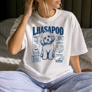 May include: A white short-sleeved t-shirt featuring a blue graphic of a Lhasapoo dog. The design includes text such as "LHASAPOO," "ADORABILITY FORMULA," "I DON'T FOLLOW COMMANDS. I NEGOTIATE," "DAILY PRIORITIES," "FLOOF LEVEL: MAXIMUM OVERLOAD," and a warning.