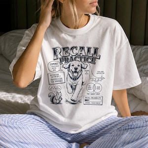 May include: A white t-shirt featuring a graphic print titled RECALL PRACTICE. The design includes a central illustration of a golden retriever, a squirrel, and various diagrams labelled with text including DISTRACTION FACTOR, THE SWEET SPOT, and RECALL RELIABILITY.