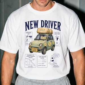 Könnte beinhalten: Ein weißes T-Shirt mit einer Grafik eines hellgrünen Autos, das ein Bündel auf dem Dach mit der Aufschrift 'PLEASE BE PATIENT' trägt. Das Auto hat Schilder mit 'STUDENT DRIVER', 'BRAKES ARE SUGGESTIONS', 'WIDE TURNS' und 'HONK IF SCARED'.