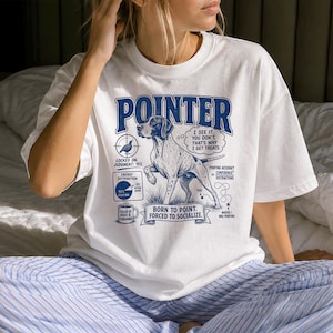 Può includere: Una t-shirt bianca a maniche corte con una grafica blu di un cane pointer. Il design include il testo POINTER, I SEE IT, YOU DON'T, THAT'S WHY I GET TREATS, BORN TO POINT, FORCED TO SOCIALIZE, insieme a vari diagrammi e grafici.