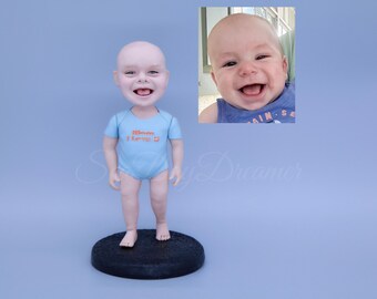 May include: A blue and orange personalized bobblehead figurine of a baby with a smiling face. The figurine is wearing a blue onesie with the text "Mom I love you".