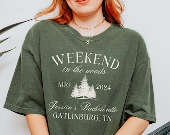 May include: A green t-shirt with the text "Weekend in the woods" and a graphic of pine trees. The text "Aug 2024" and "Jessica's Bachelorette Gatlinburg, TN" is also printed on the shirt.