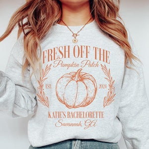 May include: A gray sweatshirt with the text "Fresh Off The Pumpkin Patch" in orange. The text is surrounded by a drawing of a pumpkin and leaves. The text "Katie's Bachelorette Savannah, GA" is also printed on the sweatshirt.