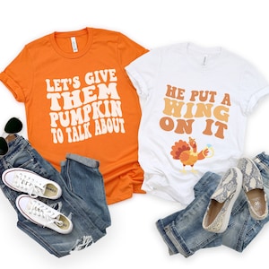 May include: Two t-shirts with Thanksgiving-themed text and graphics. The orange shirt says "Let's give them pumpkin to talk about." The white shirt says "He put a wing on it" and features a cartoon turkey holding a ring.