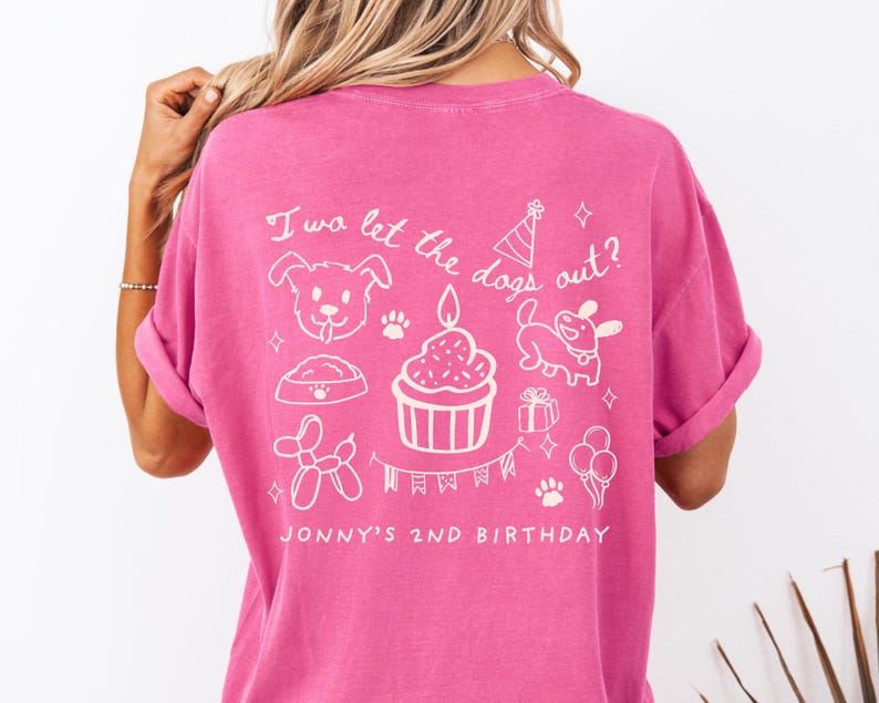 以下が含まれることがあります： 背面に白いグラフィックデザインが施されたピンク色のTシャツ。デザインには犬、カップケーキ、パーティーハット、「I wa let the dogs out?」と「Jonny's 2nd Birthday」の文字が含まれています。