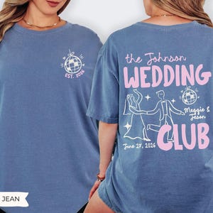 May include: Blue jean-colored t-shirt with a white and pink graphic design. The front features a disco ball design with "EST. 2026". The back displays "the Johnson WEDDING CLUB" with a dancing couple illustration, date, and names.