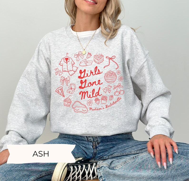 Puede incluir: Una sudadera gris con un dise&ntilde;o gr&aacute;fico rojo que dice "Girls Gone Mild" e incluye una variedad de ilustraciones, incluyendo un par de chanclas, una caja de regalo, un cupcake y una flor. El texto "Madison's Bachelorette" tambi&eacute;n est&aacute; incluido en el dise&ntilde;o.